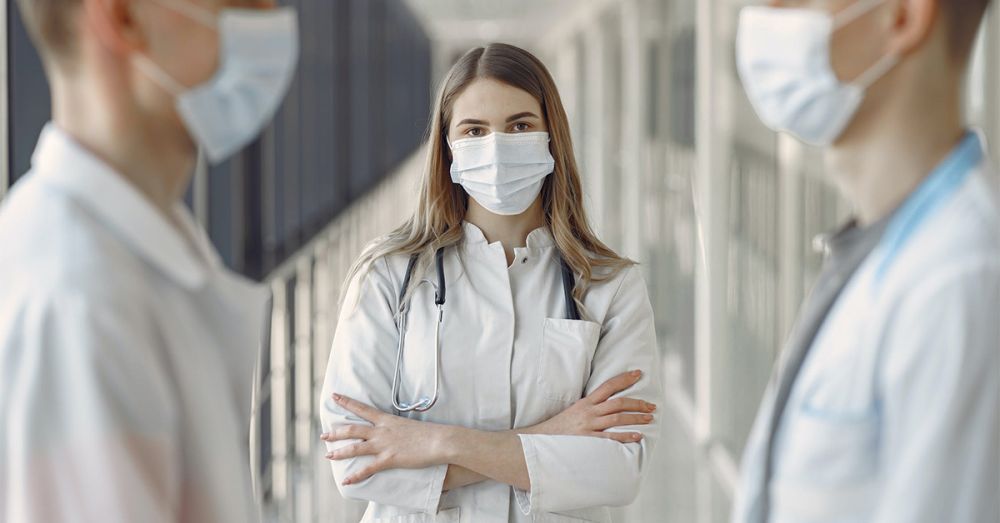 concerned looking nurse with face mask on and arms crossed with colleagues