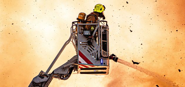 Fire fighter on crane with hose battling fire