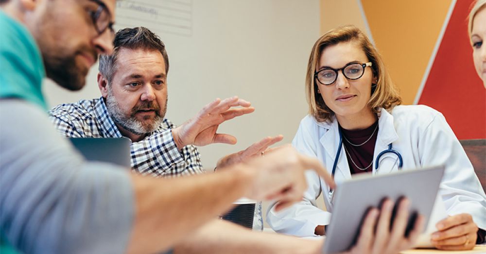 health workers at a table discussing information on an ipad or tablet