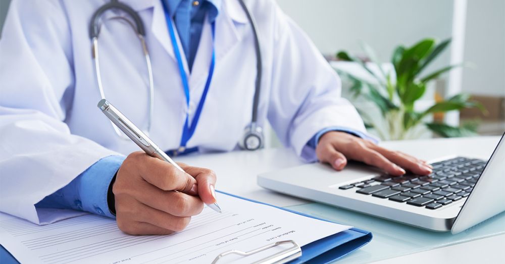 doctor at his desk looking at his laptop making notes